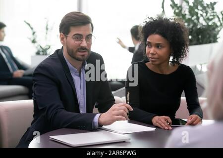 Assistant watching young confident businessman discussing contract terms with clients. Stock Photo