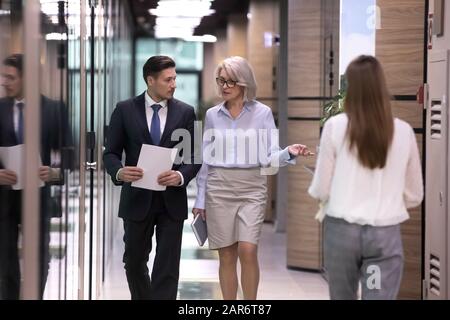 Different ages focused international company workers walking in corridor. Stock Photo