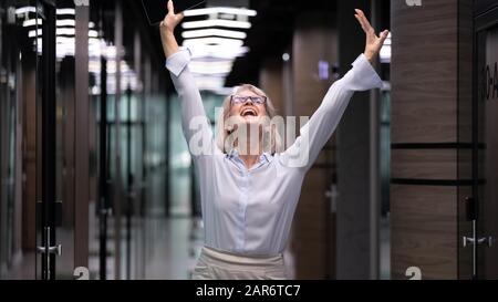 Overjoyed middle aged businesswoman celebrating outstanding job results. Stock Photo
