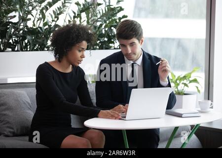 Multiracial employees discussing project ideas, working on laptop together. Stock Photo