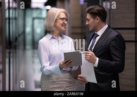 Happy different ages workers discussing working issues in corridor. Stock Photo