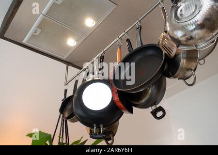 Stainless steel cookware , kitchenware set hanging on a rack on the wall, frying pans and saucepan in modern home Stock Photo