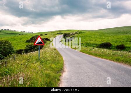 Warning traffic sign along a steep winding road in the Scottish countryside on a cloudy spring day Stock Photo