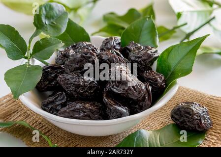 bowl of sweet dried plums with lemon leaves on a white background Stock Photo