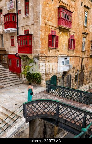 Old city of Valletta in Malta, traditional houses with balconies, pedestrian bridge over Liesse street and the Bridge Bar on the corner. Stock Photo