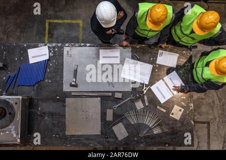 Team of workers and foreman look at documents and blueprints on table at factory top view Stock Photo