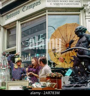 London 1970s, two women having fun with merchant while shopping at antiques store, Kensington, England, UK, GB, Great Britain, Stock Photo