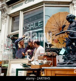 London 1970s, two women having fun with merchant while shopping at antiques store, Kensington, England, UK, GB, Great Britain, Stock Photo