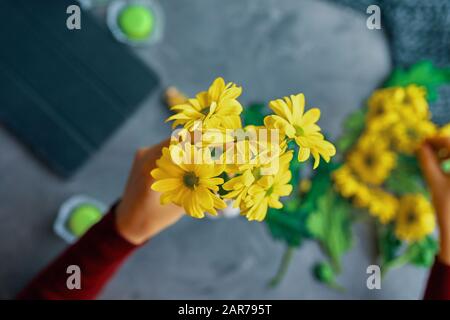 Woman puts a yellow chrysanthemum flowers in a glass transparent vase on the loft table