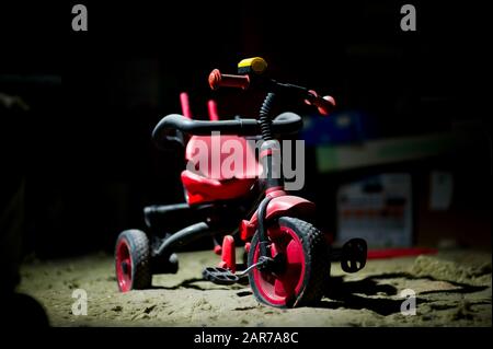 an abandoned red children's tricycle stands under a layer of dust in the basement among a variety of junk. The concept of forgotten childhood. Close u Stock Photo