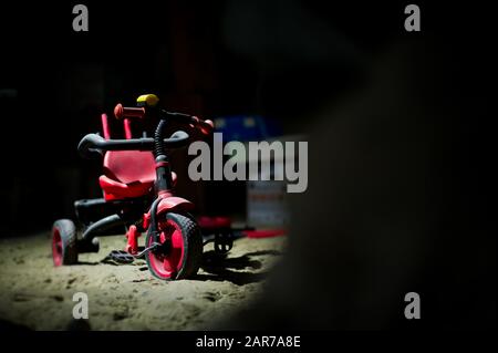 an abandoned red children's tricycle stands under a layer of dust in the basement among a variety of junk and garbage. The concept of sad childhood, l Stock Photo