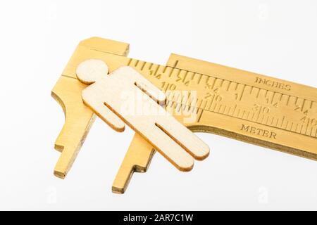 Macro small laser-cut wooden figure & brass calipers against off-white BG. Measuring personal performance indicators, demographics, productivity, Stock Photo