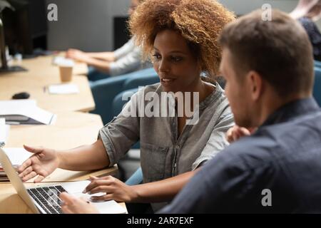 Ethnic female employee collaborating with male colleague in shared office Stock Photo