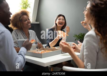 Smiling multiethnic colleagues have fun eating pizza in office Stock Photo