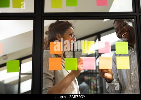 Smiling multiethnic colleagues collaborate project on sticky notes Stock Photo