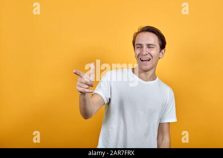man in white t-shirt smiling and showing finger direction on yellow background Stock Photo