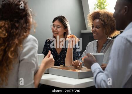 Overjoyed multiracial colleagues have fun enjoying pizza break in office Stock Photo