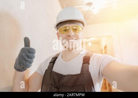 Builder worker man happy makes selfie photo with safety glasses and white helmet Stock Photo