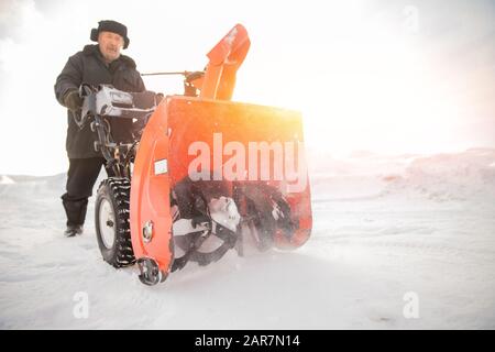 Man cleaning snow from sidewalks with snowblower machine winter Stock Photo