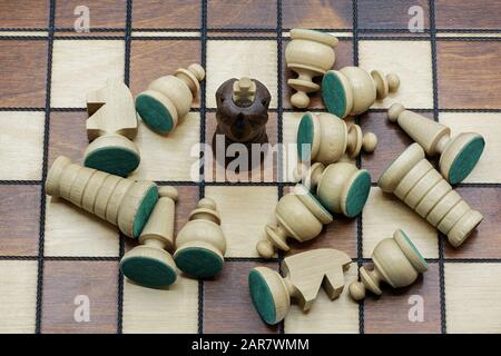 Survival Concept: Black King Chess Piece Surrounded By Defeated White Chess Pieces On A Wooden Chess Board Stock Photo