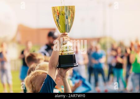 Happy kids in school sports team rising golden cup. Boys winning sports championship. Child holding big golden trophy Stock Photo