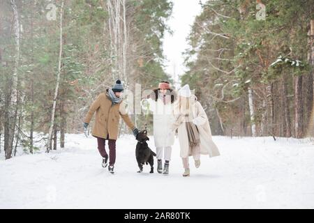 Black retriever playing with group of happy young friends running down road Stock Photo