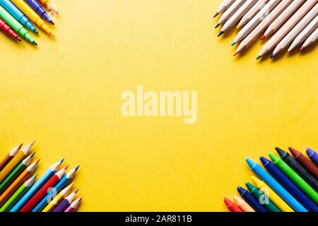 Yellow minimalistic background with colorful sharpened pencils, felt-tip pen and crayons in the corners Stock Photo