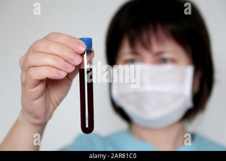 Test tube in female hand close up, woman in medical mask holding a vial with red liquid. Concept of blood sample, vaccination, coronavirus outbreak Stock Photo