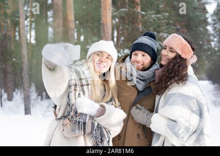 Three cheerful and affectionate friends looking at smartphone camera with smiles Stock Photo