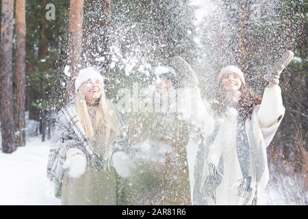 Group of young cheerful friends in winterwear throwing snow while having fun Stock Photo