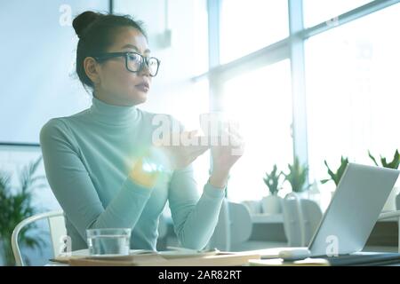 Young Asian businesswoman in casualwear having cup of tea or coffee Stock Photo