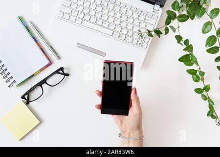 Modern workplace in white color with woman hand using mobile phone in office. Top view. Flat lay. Stock Photo