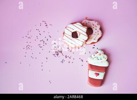 Fragrant gingerbread in the form of doughnuts on a pink background with sequins of small multi-colored stars and donut inscription. Flat lay Stock Photo