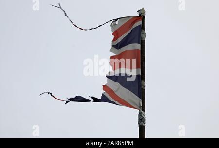 Union Jack, UK flag, tattered, torn, flying and fluttering on a grey pole with grey sky could illustrate a disaster such as a war, storm or Brexit. Stock Photo