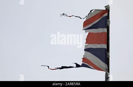 Union Jack, UK flag, tattered, torn, flying and fluttering on a grey pole with grey sky could illustrate a disaster such as a war, storm or Brexit. Stock Photo