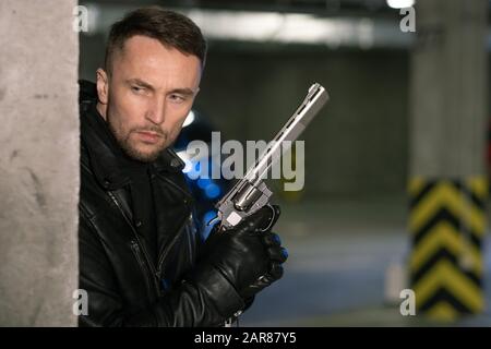 Young killer or agent holding gun and getting ready to shoot victim or criminal Stock Photo