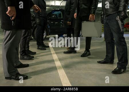 Two rows of men in black with handguns and suitcase standing on parking area Stock Photo