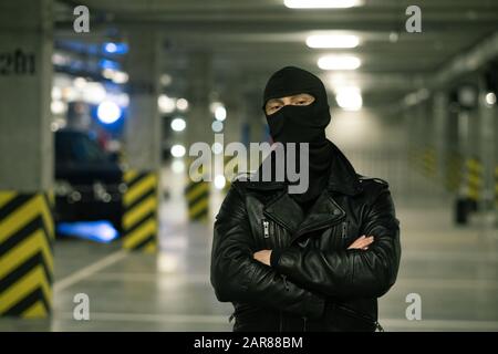Criminal in black leather jacket and balaclava on head crossing arms by chest Stock Photo