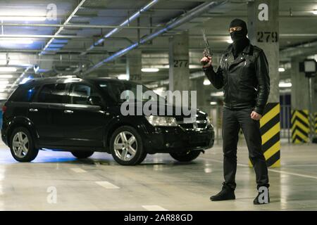 Terrorist or gangster in black jacket and balaclava on head holding handgun Stock Photo