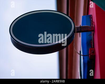 Oval real sign on wall of building. Dark blue rounded signboard of cafe, restaurant or shop on city street on wall of old mansion or stone building. M Stock Photo