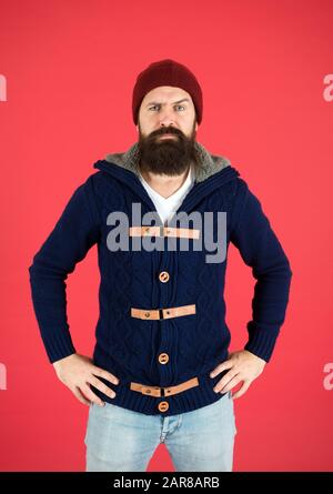 Brutal temper. Fashion menswear shop. Masculine clothes concept. Winter menswear. Clothes design. Man bearded warm jumper and hat red background. Winter season menswear. Warm and comfortable. Stock Photo