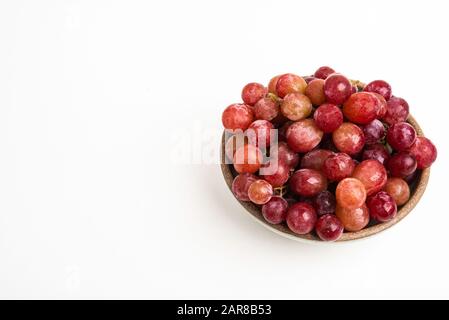 A bunch of fresh red grapes bunched on a small ceramic bowl set on a plain white background. Stock Photo