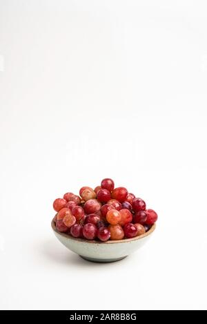 A bunch of fresh red grapes bunched on a small ceramic bowl set on a plain white background. Stock Photo