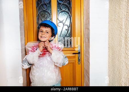 Boy fasten helmet wear super safe bubble wrap have overprotective mother standing near home door Stock Photo