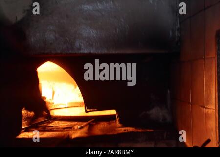 A pizzaiolo man cooks a chickpeas in a burning flame wood oven Stock Photo