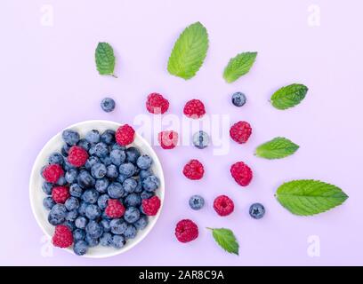 Flat lay composition of bowl with raspberries and blueberries and plenty of different berries on a pink background and fresh green mint leaves as a de Stock Photo
