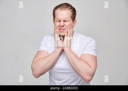 A man in a white T-shirt holds on to his jaw. The concept of toothache. Close up. Stock Photo