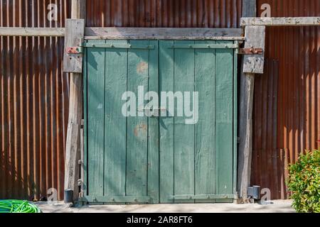 Exterior sunny front view of old vintage  warehouse with rough wooden green slide doors and rusty corrugated iron wall with vertical pattern. Stock Photo