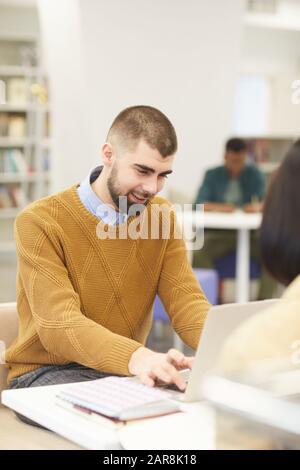 Portrait of smiling young man using laptop while studying in college library with other people in background, copy space Stock Photo