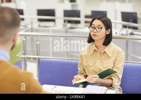 Portrait of Asian young woman studying in college library and looking up at her partner in modern interior, copy space Stock Photo